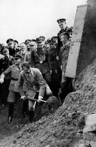 Auf dem Foto ist zu sehen, wie Adolf Hitler den ersten Spatenstich setzt.